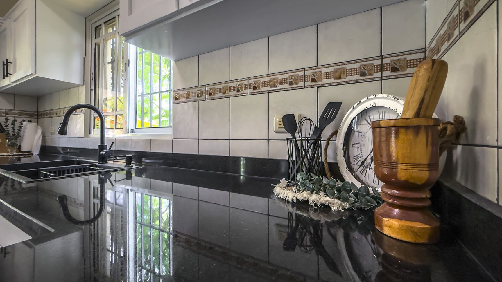 Modern kitchen counter with sink, faucet, utensils, clock, and mortar and pestle.