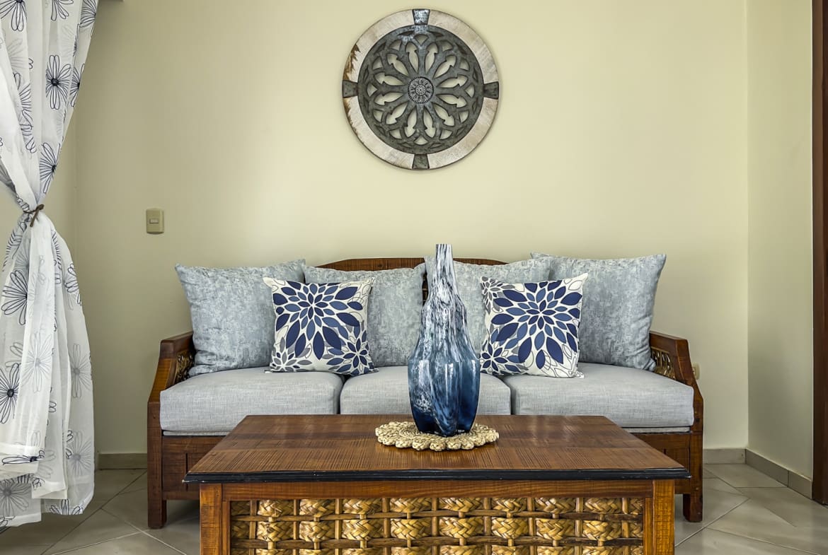 Living room with grey sofa, blue floral pillows, and a woven coffee table.