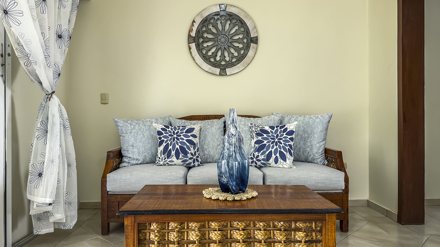 Living room with grey sofa, blue floral pillows, and a woven coffee table.