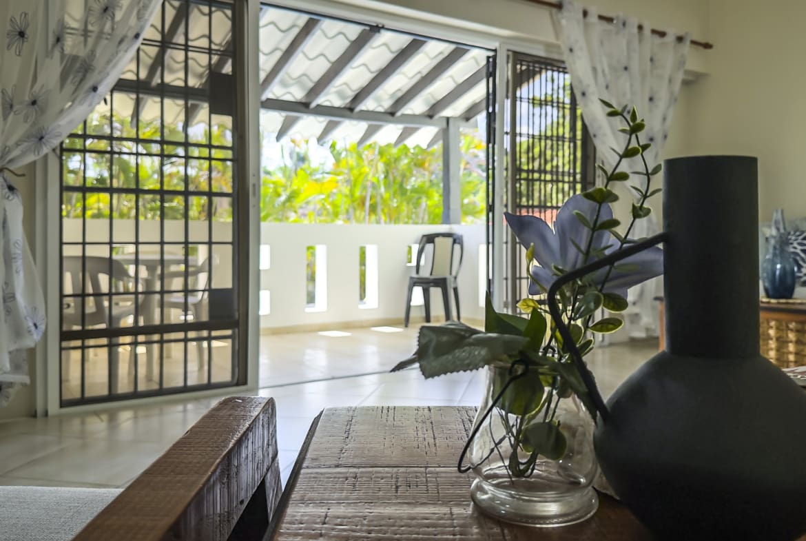Interior view of a modern tropical villa with sliding doors opening to a sunny patio and lush greenery.