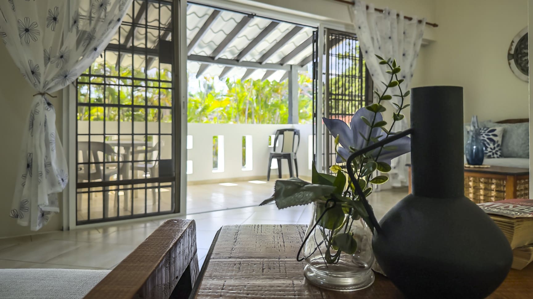 Interior view of a modern tropical villa with sliding doors opening to a sunny patio and lush greenery.