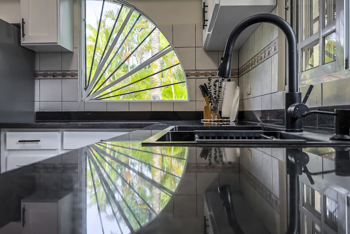 Modern kitchen sink with black granite countertops and a unique fan-shaped window.