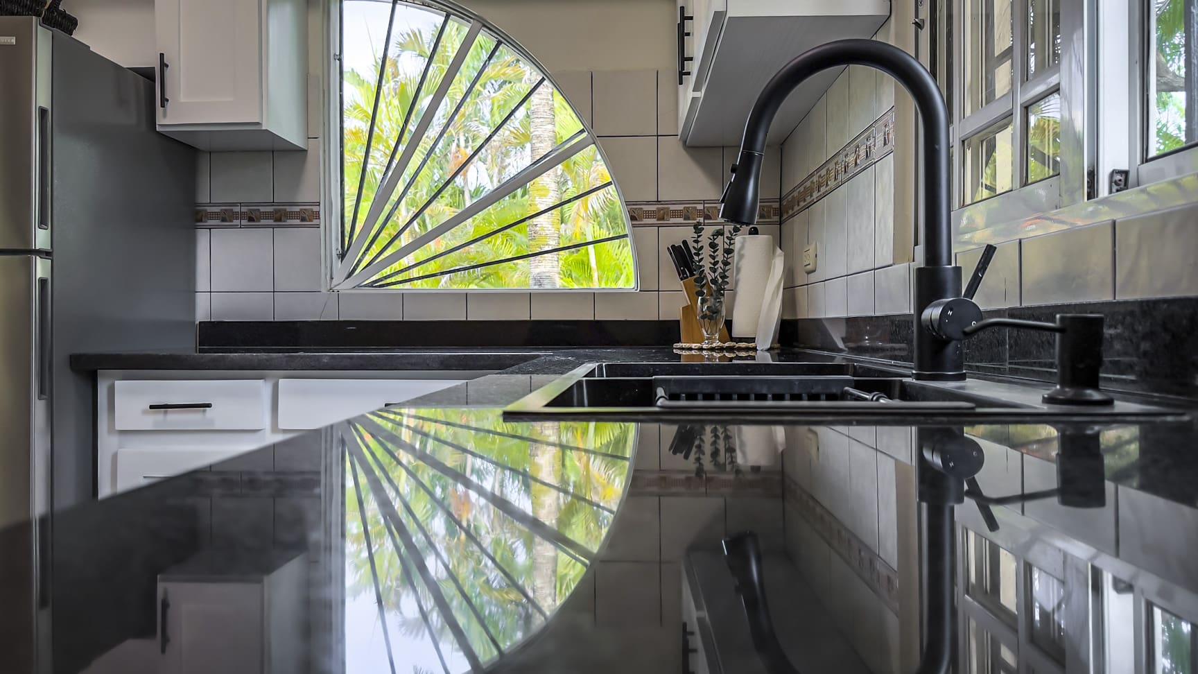 Modern kitchen sink with black granite countertops and a unique fan-shaped window.
