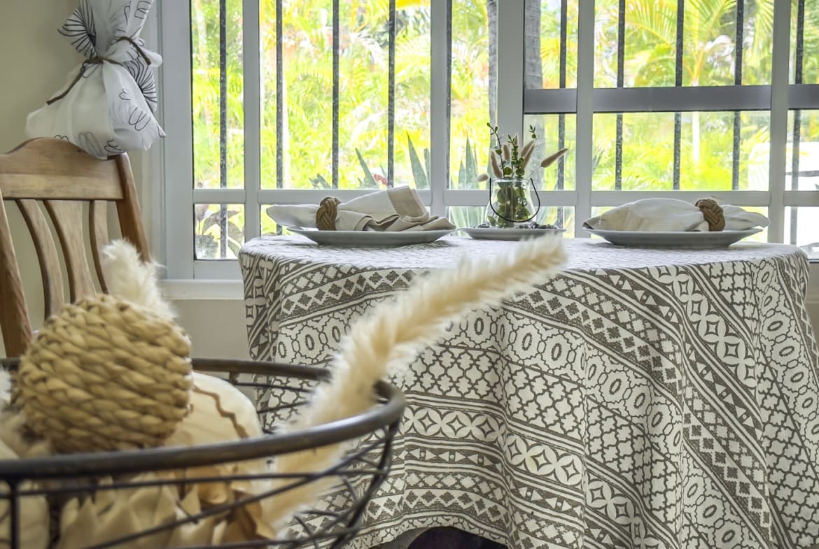 Dining table set for two with a patterned tablecloth and view of lush greenery