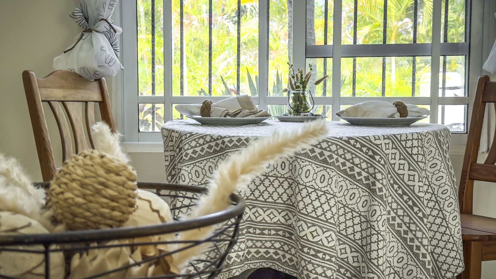 Dining table set for two with a patterned tablecloth and view of lush greenery