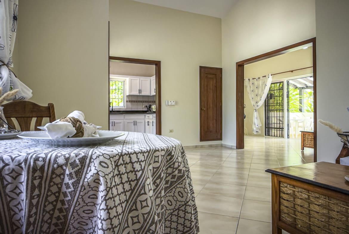 Dining area with a table set for a meal, opening to a bright kitchen and patio.