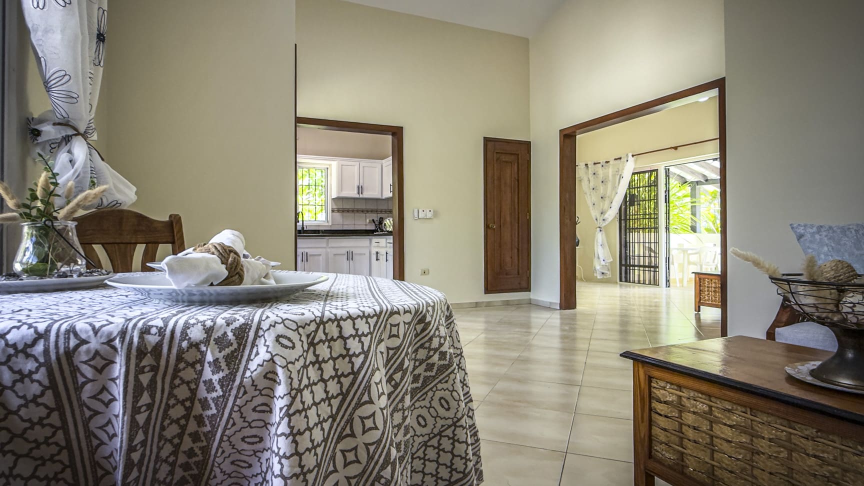 Dining area with a table set for a meal, opening to a bright kitchen and patio.