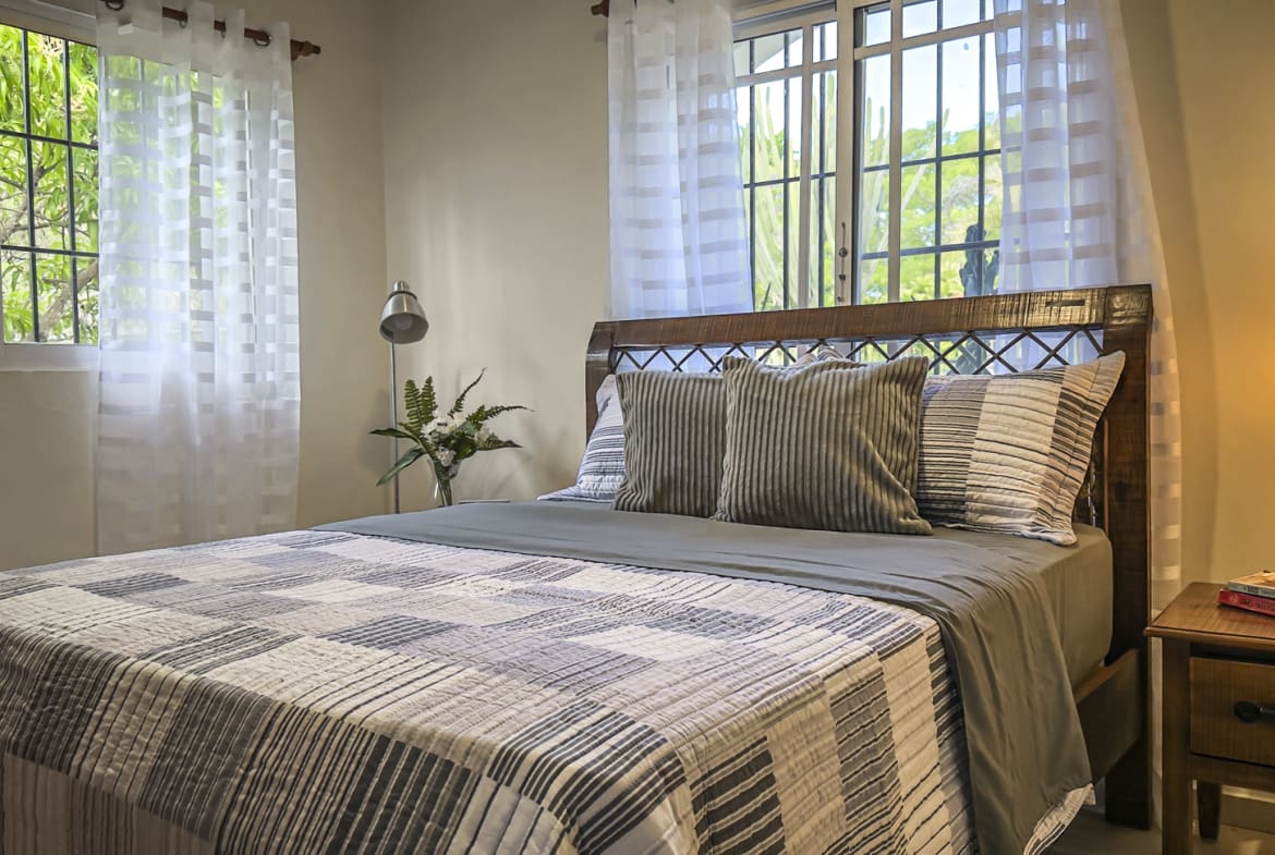 Cozy bedroom with a queen-size bed, striped bedding, and large windows with sheer curtains.