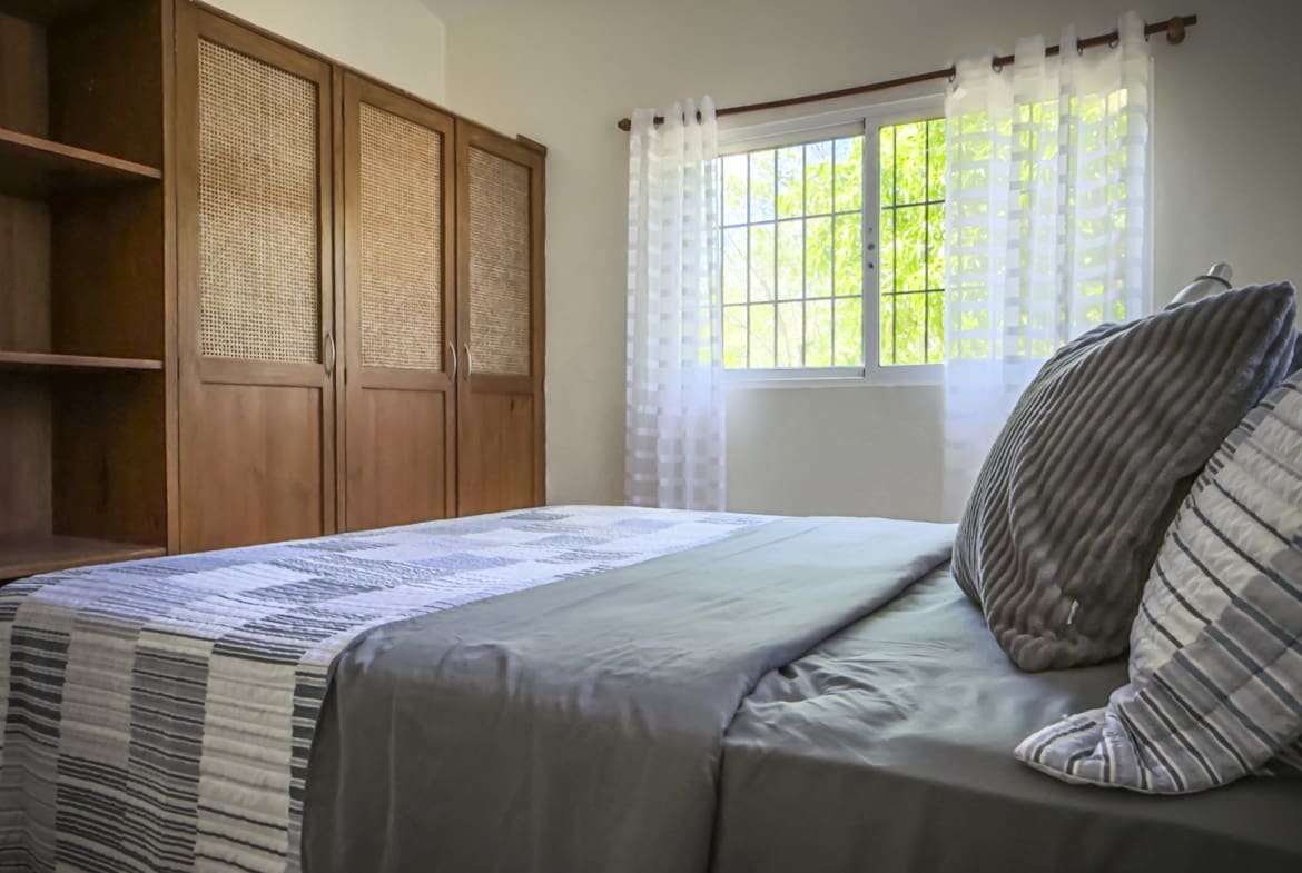 Modern bedroom with wooden wardrobe, patterned bedding, and green window view