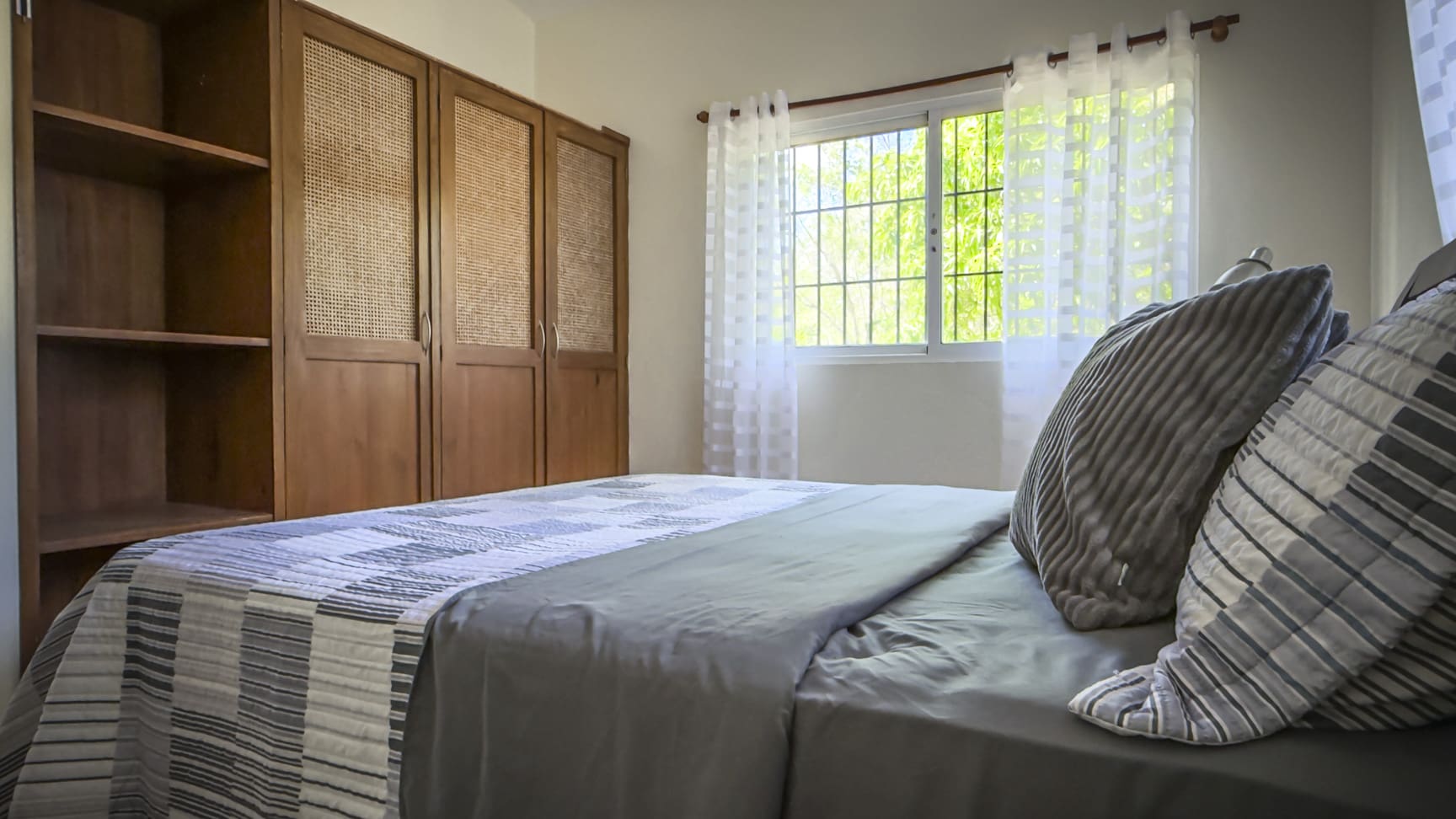 Modern bedroom with wooden wardrobe, patterned bedding, and green window view
