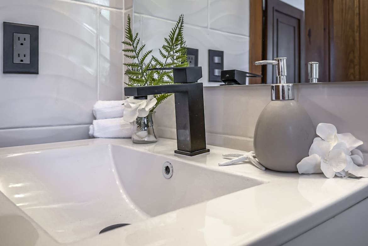 Modern bathroom sink with black faucet, soap dispenser, and white flowers