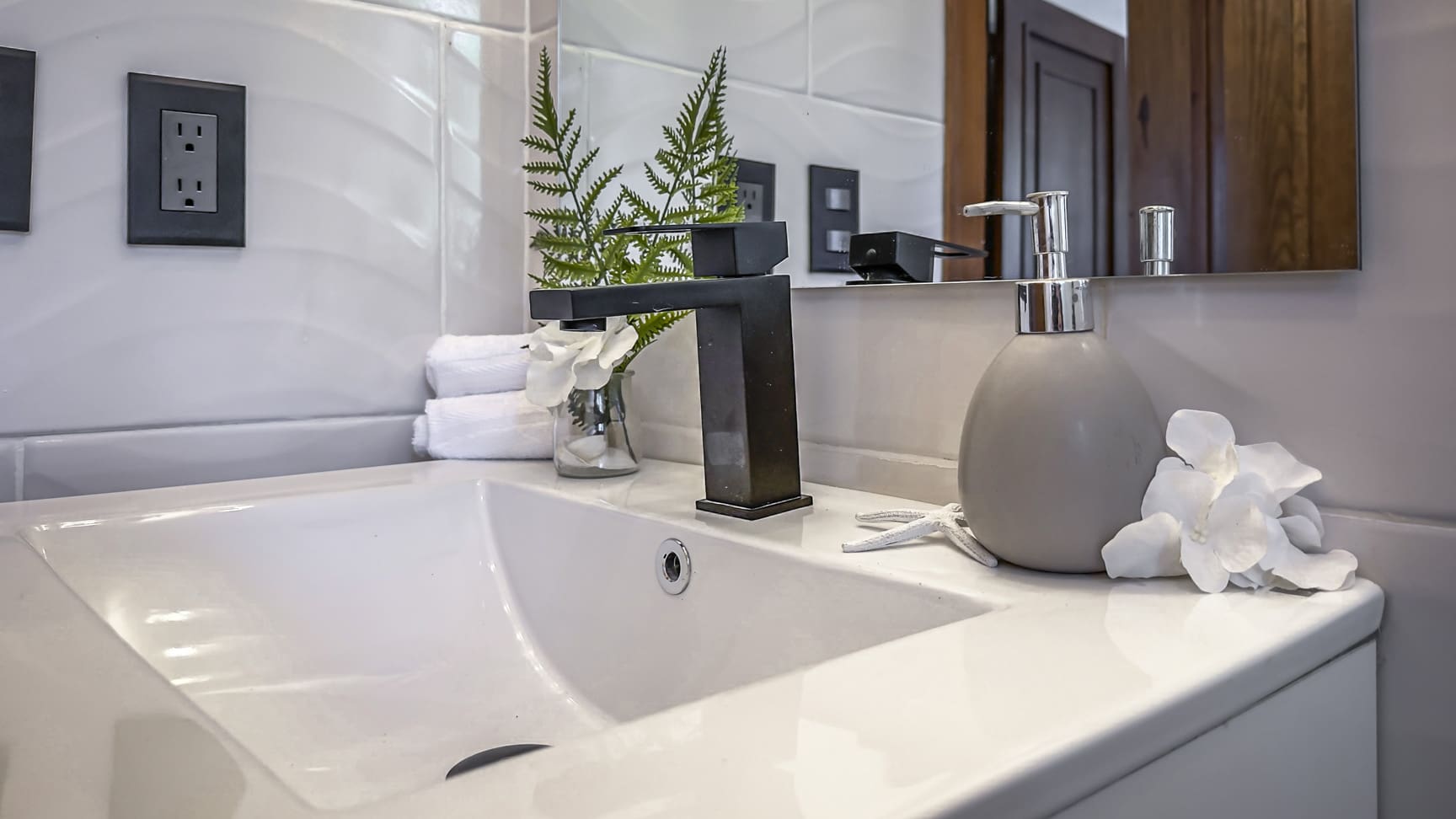 Modern bathroom sink with black faucet, soap dispenser, and white flowers
