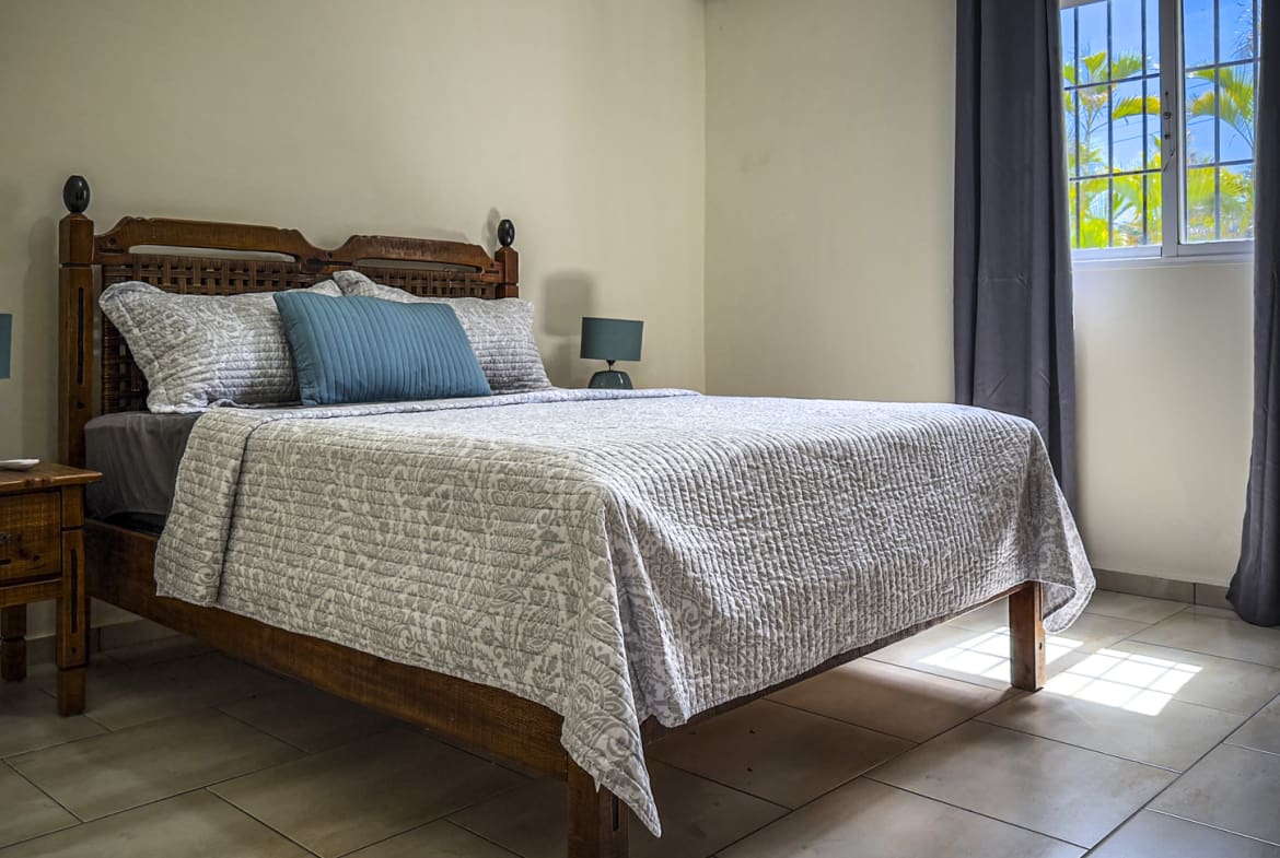 Cozy bedroom with a queen-size bed, bedside table, and window with tropical view.
