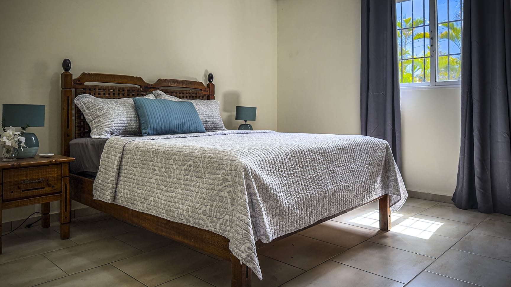 Cozy bedroom with a queen-size bed, bedside table, and window with tropical view.