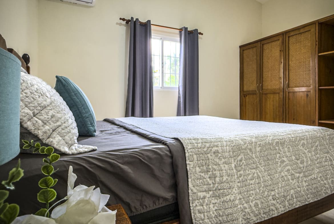 Cozy bedroom with queen bed, blue and white pillows, and wooden wardrobe.