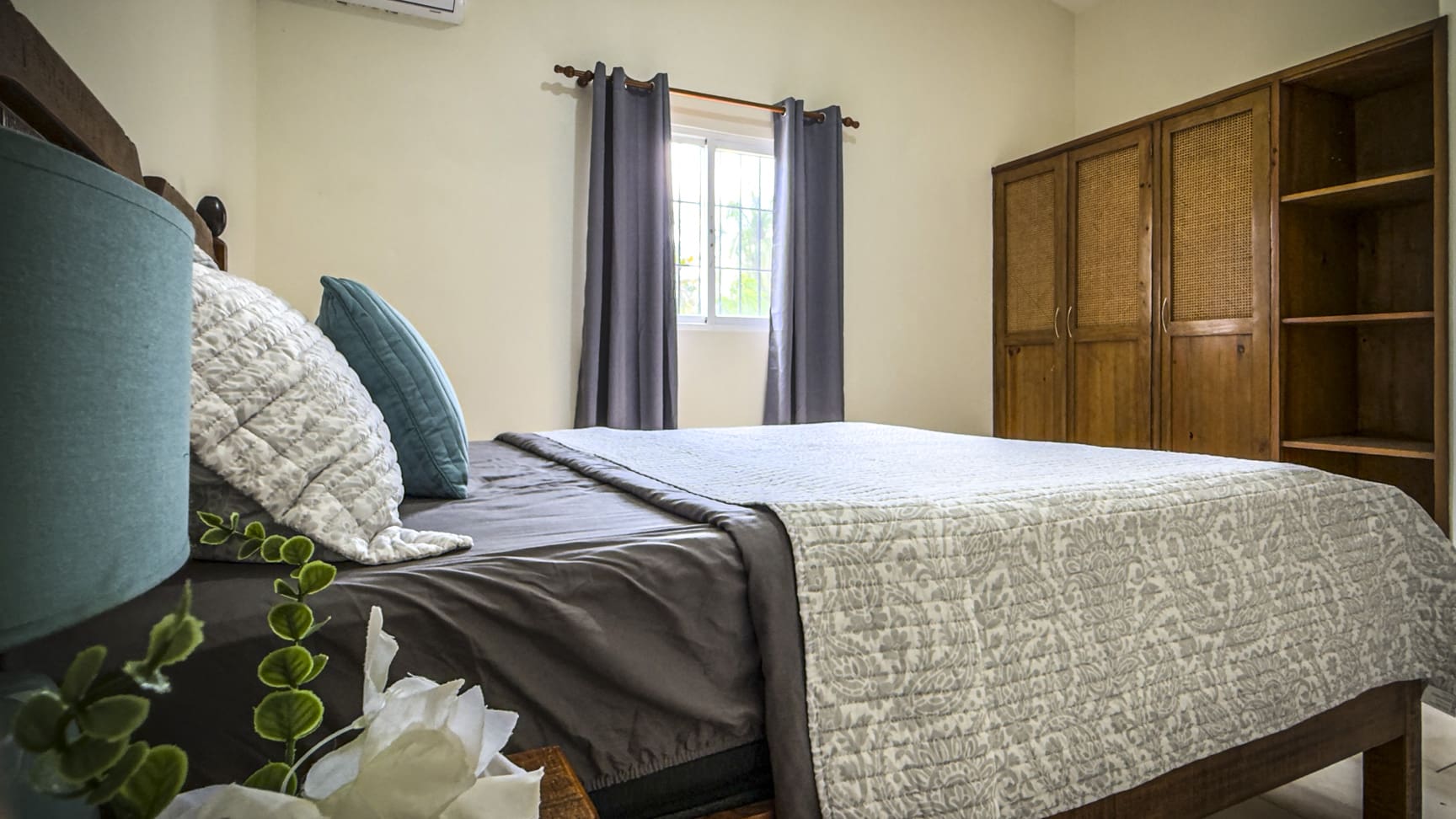Cozy bedroom with queen bed, blue and white pillows, and wooden wardrobe.