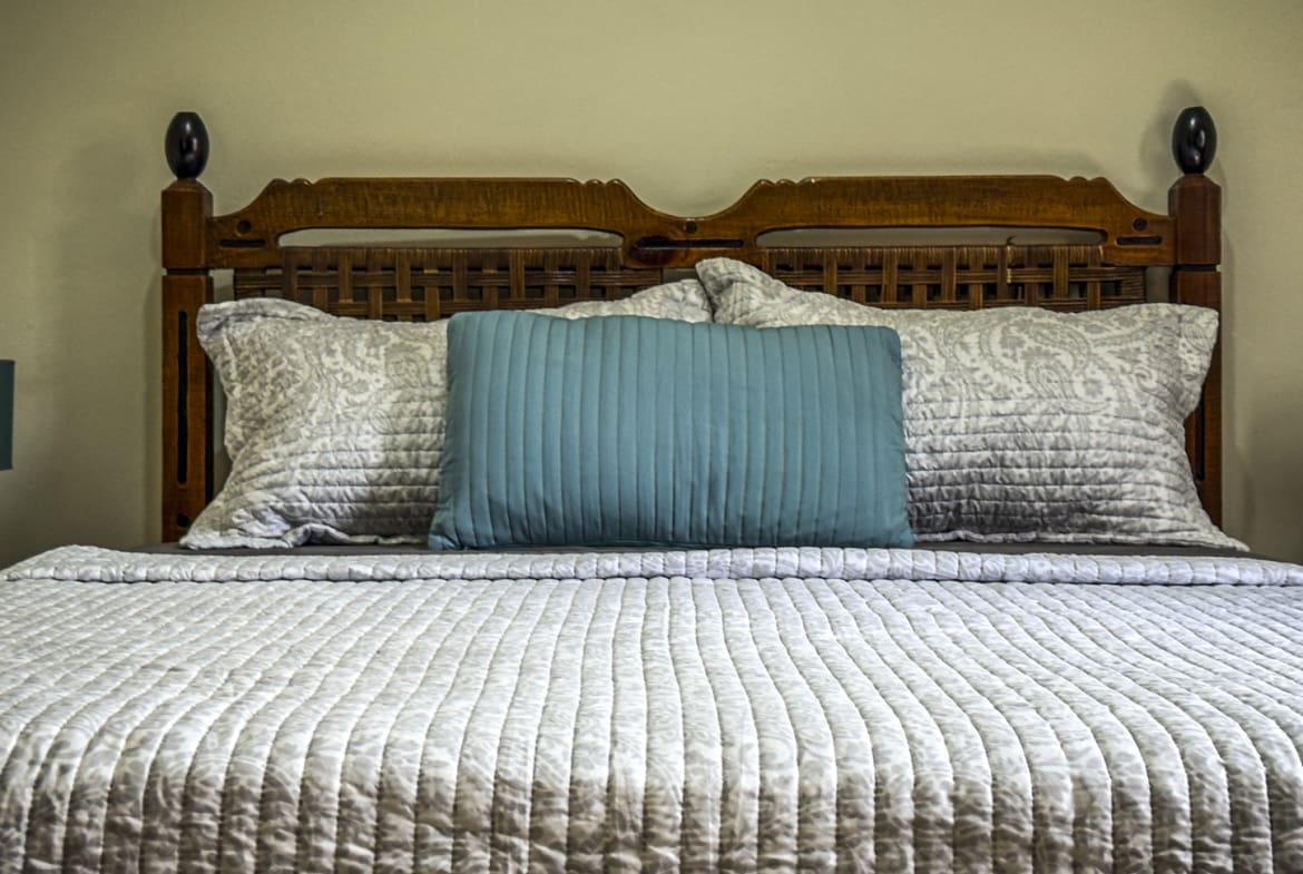 Comfortable bed with quilted white bedding, decorative pillows, and a wooden headboard.