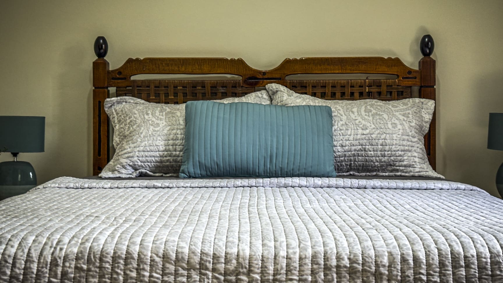 Comfortable bed with quilted white bedding, decorative pillows, and a wooden headboard.