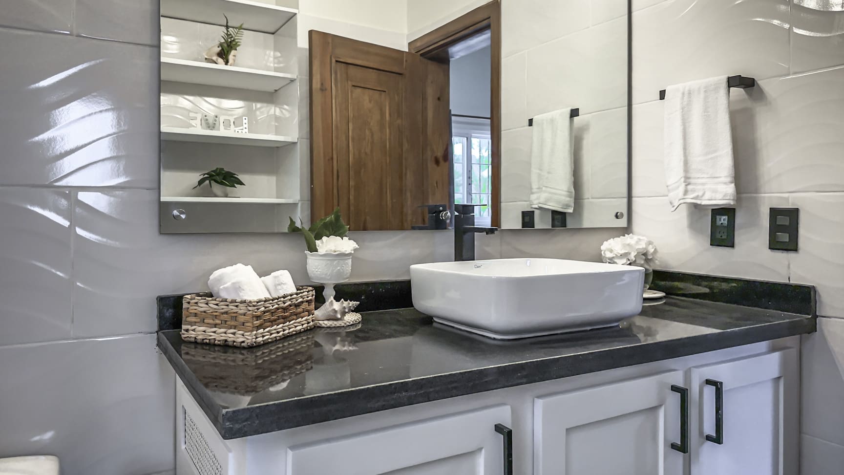 Modern bathroom vanity with white square vessel sink, black faucet, and white towels.