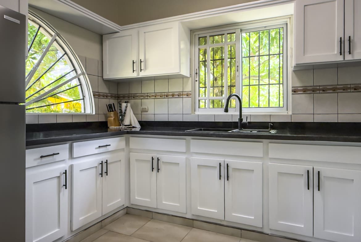 White kitchen cabinets and black countertops with a sink and window view.