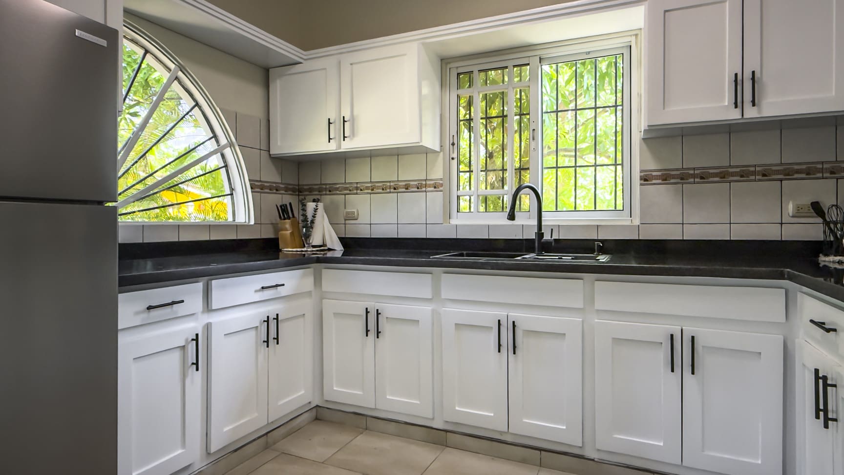 White kitchen cabinets and black countertops with a sink and window view.