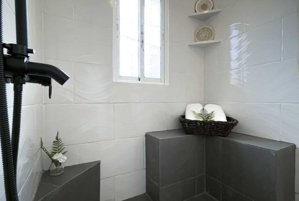 Modern shower stall with black fixtures, white wave tiles, and a small plant.