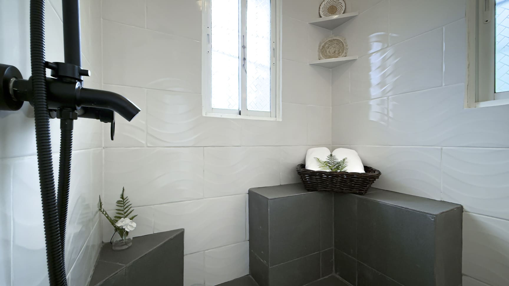 Modern shower stall with black fixtures, white wave tiles, and a small plant.