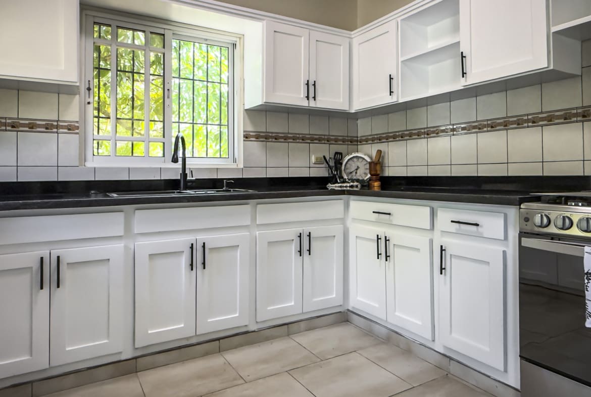 Modern white kitchen with stainless steel appliances and a window view.