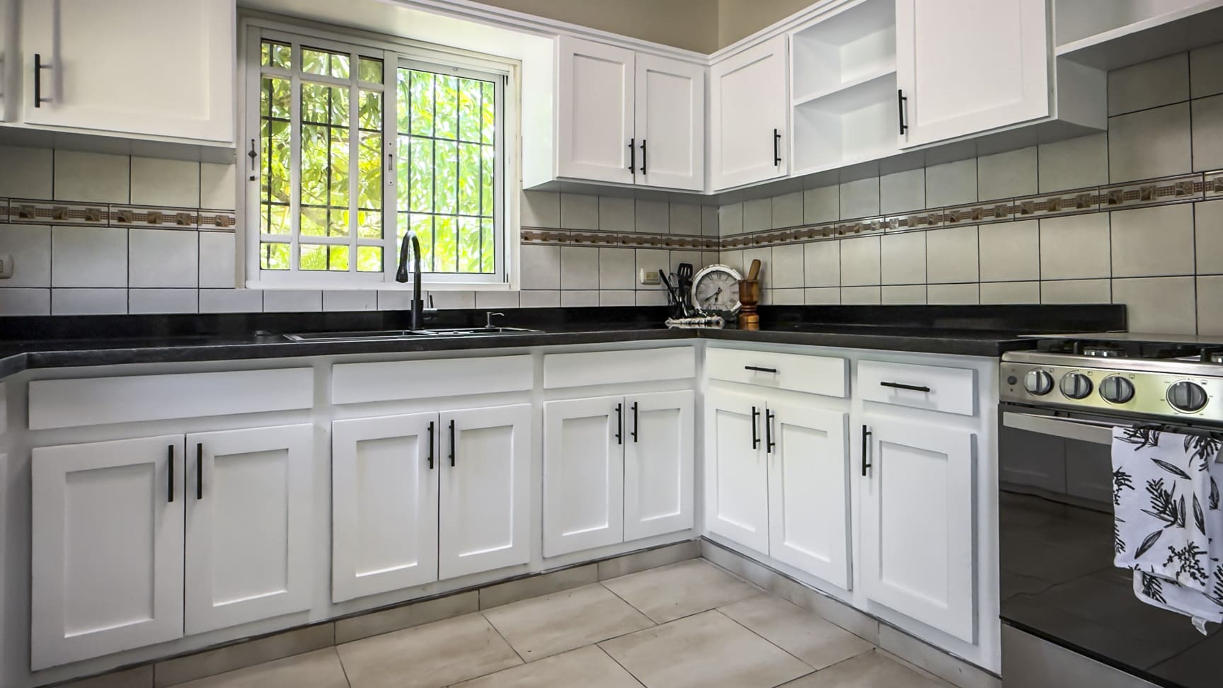 Modern white kitchen with stainless steel appliances and a window view.