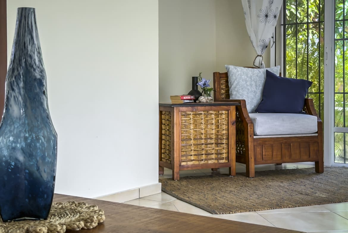 Blue glass vase on table next to wicker accent table and armchair.