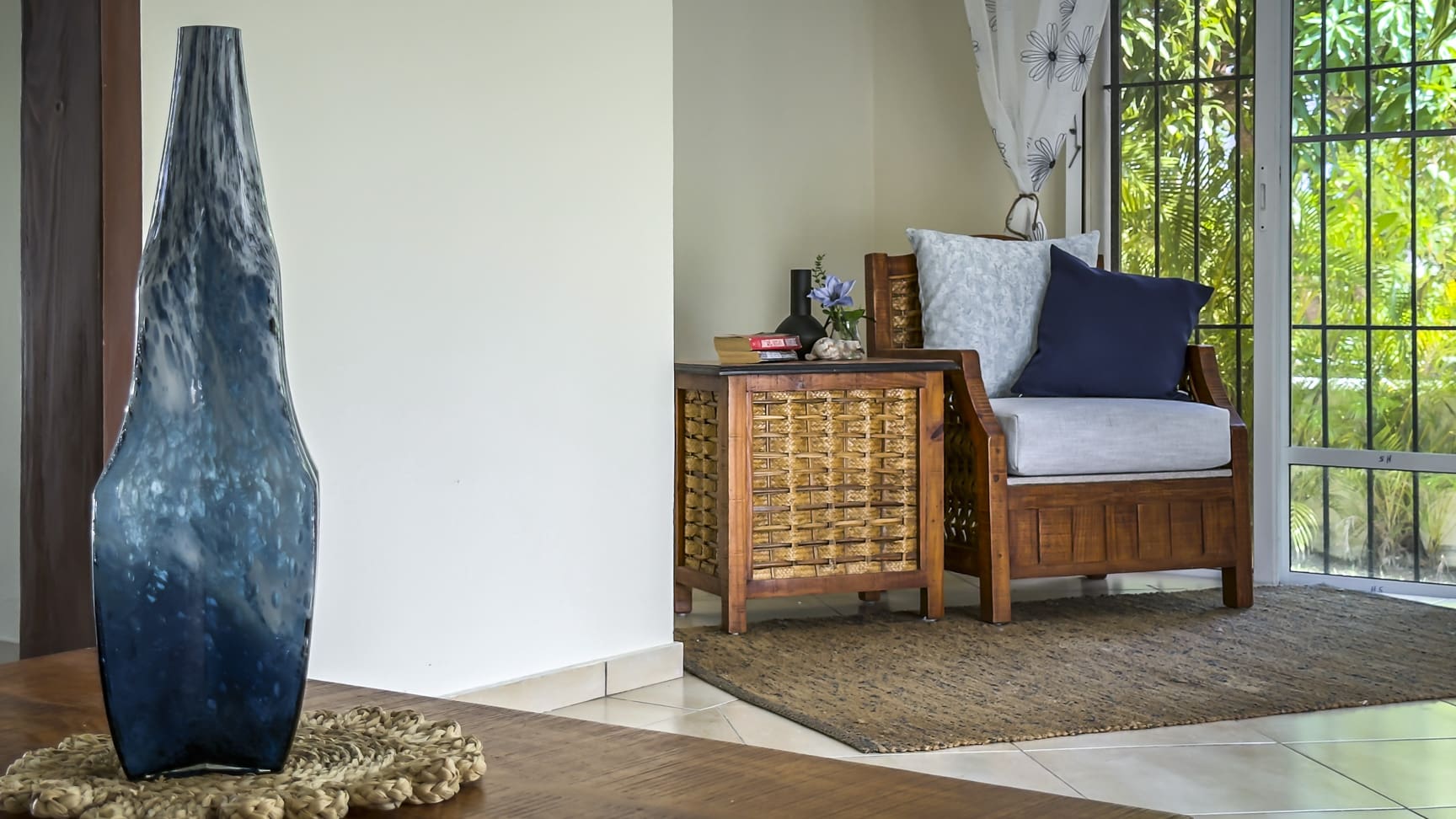 Blue glass vase on table next to wicker accent table and armchair.