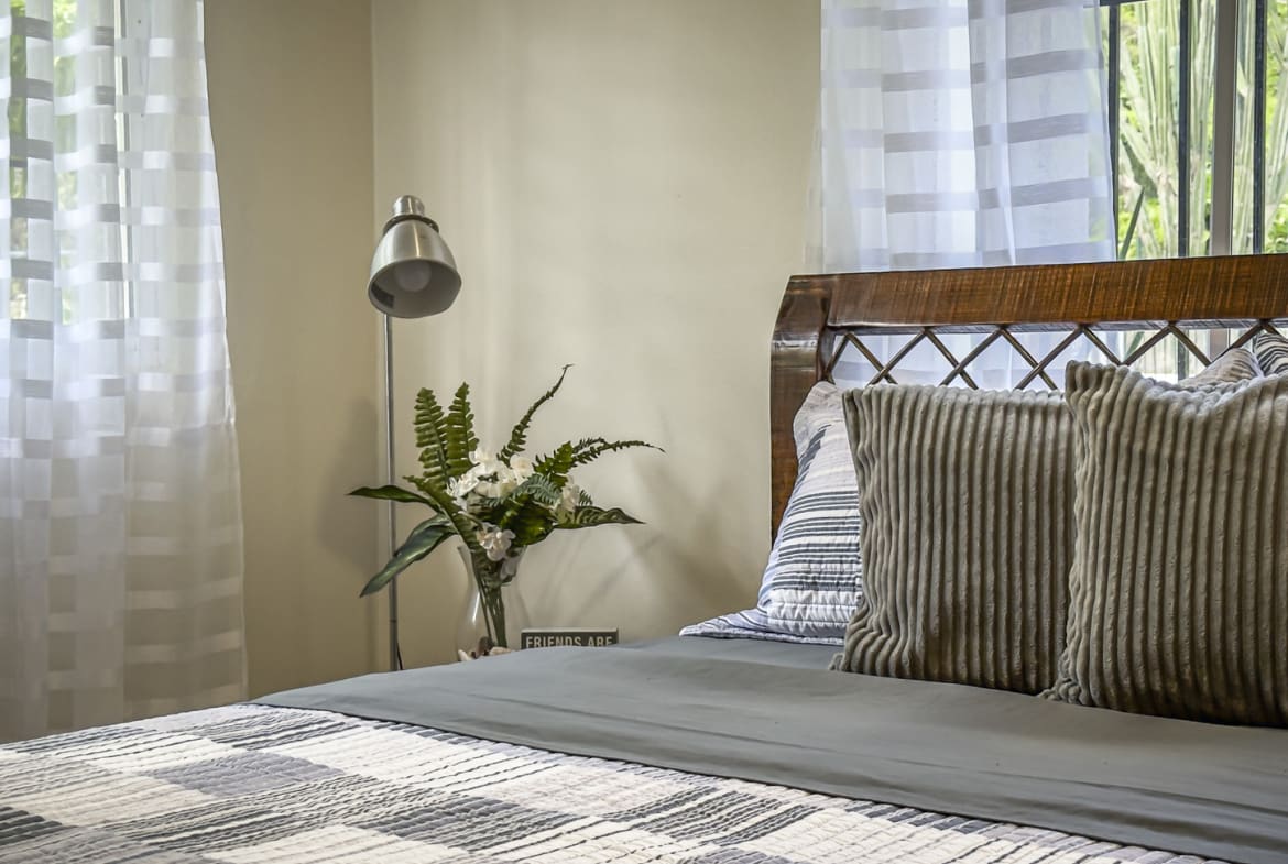 Cozy bedroom with a bed, pillows, a lamp, and sheer curtains.