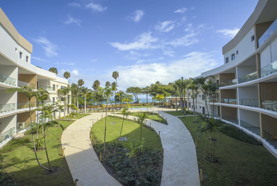 Modern resort courtyard with palm trees, curving pathways, and ocean view