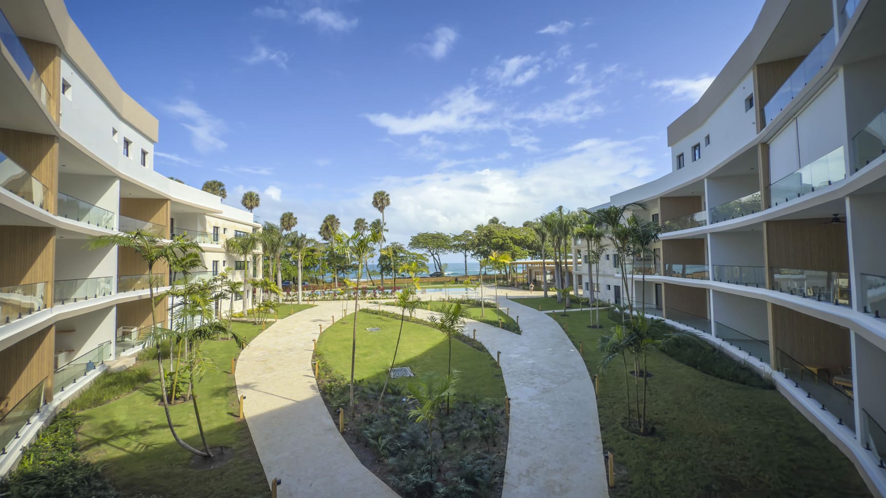 Modern resort courtyard with palm trees, curving pathways, and ocean view
