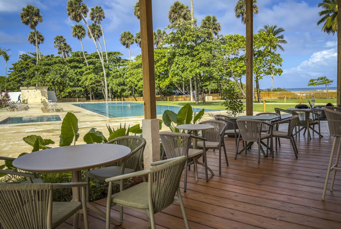 Outdoor dining area with tables and chairs overlooking a swimming pool and palm trees