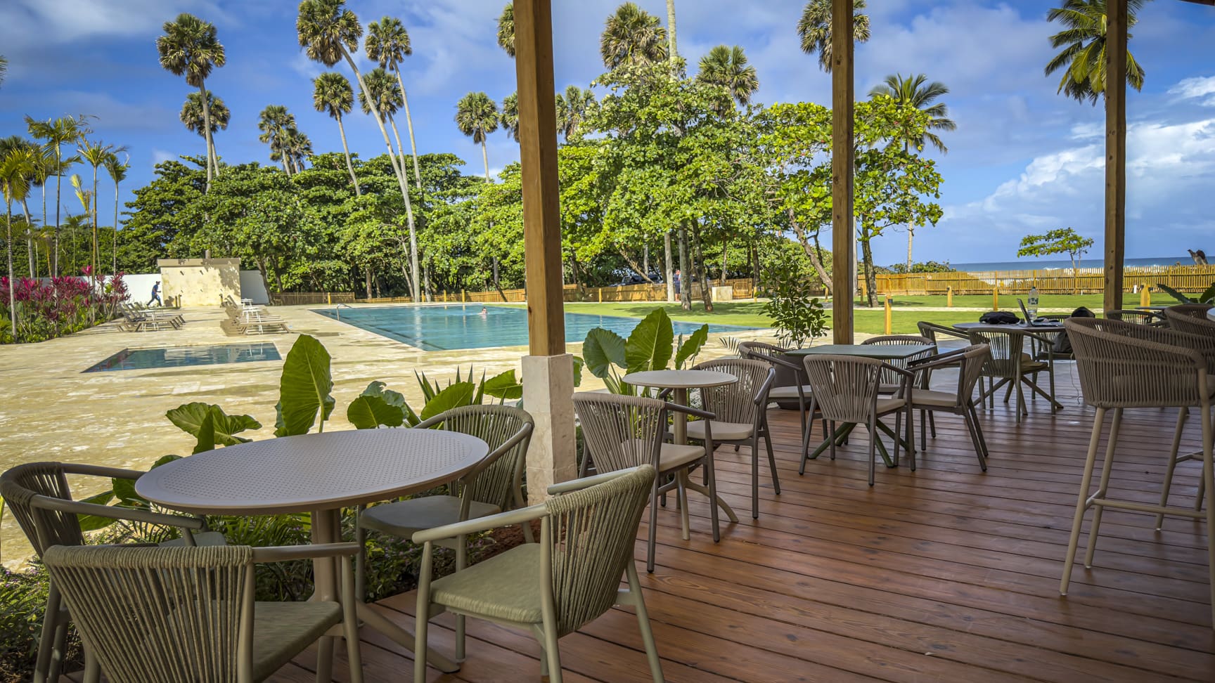 Outdoor dining area with tables and chairs overlooking a swimming pool and palm trees