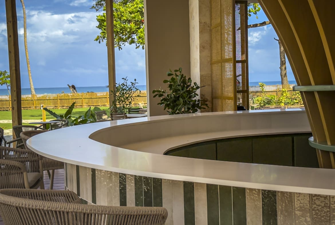 Modern bar with ocean view, featuring a curved counter and tropical plants.
