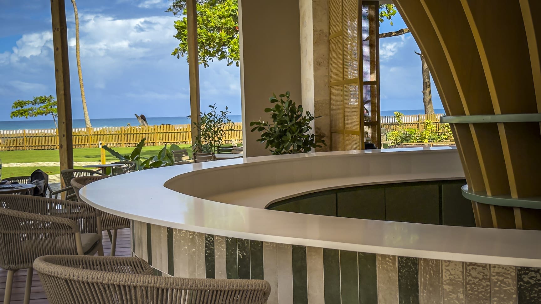 Modern bar with ocean view, featuring a curved counter and tropical plants.