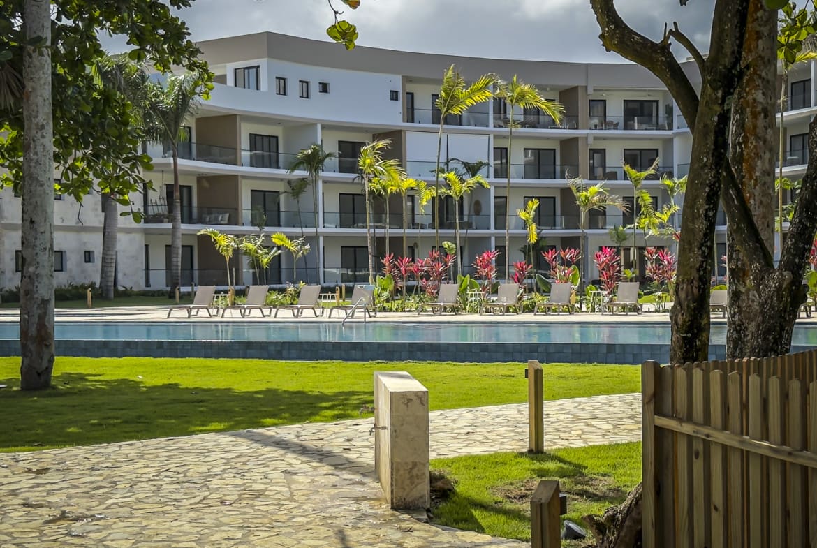 Modern resort with pool, lounge chairs, palm trees, and tropical plants.