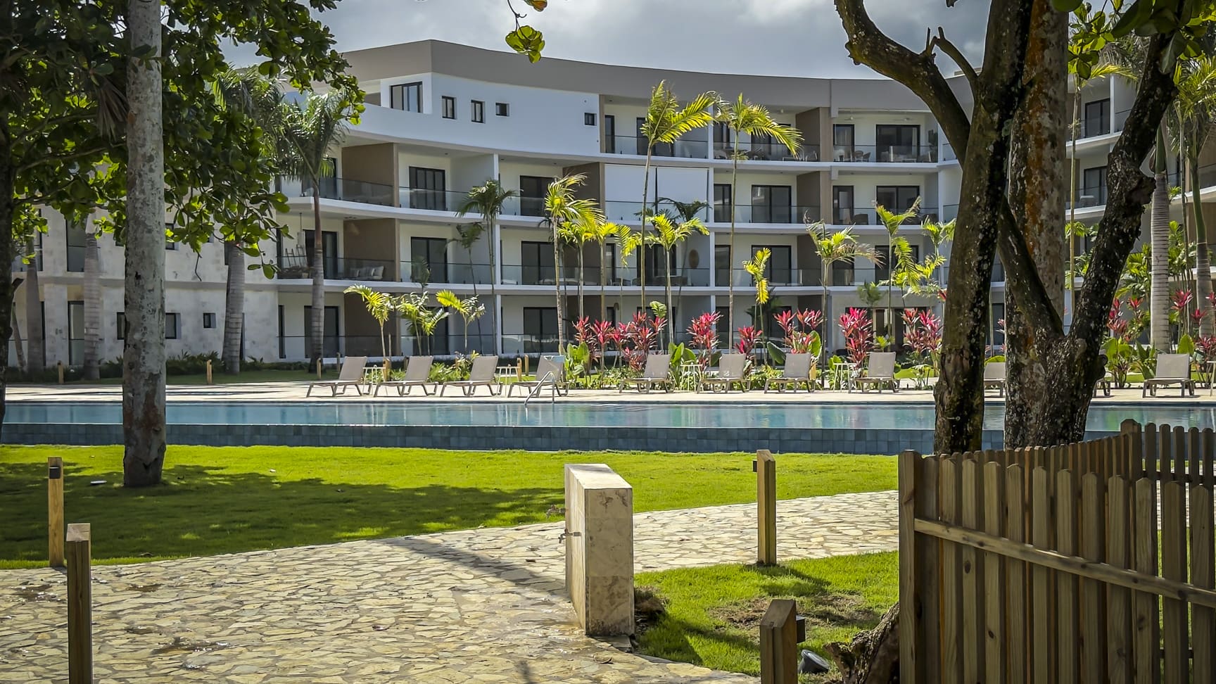 Modern resort with pool, lounge chairs, palm trees, and tropical plants.