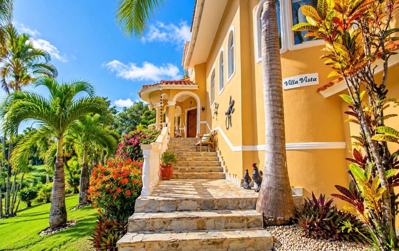 Villa Vista: Tropical luxury home entrance with palm trees and vibrant flowers.