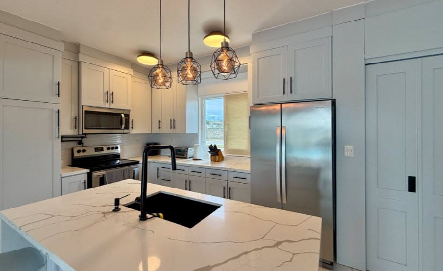 Modern kitchen island with quartz countertop and black sink, stainless steel appliances, and pendant lights.