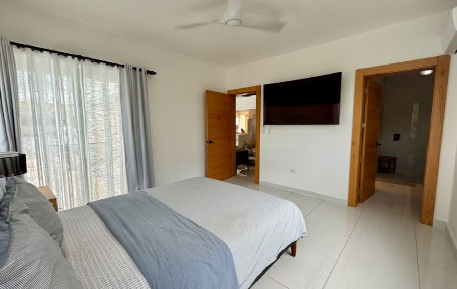 Modern bedroom with king-size bed, ceiling fan, and wall-mounted TV.