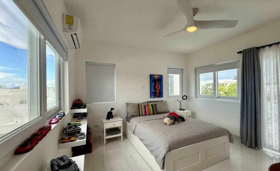 Modern bedroom with a bed, ceiling fan, and large windows overlooking a sunny landscape.