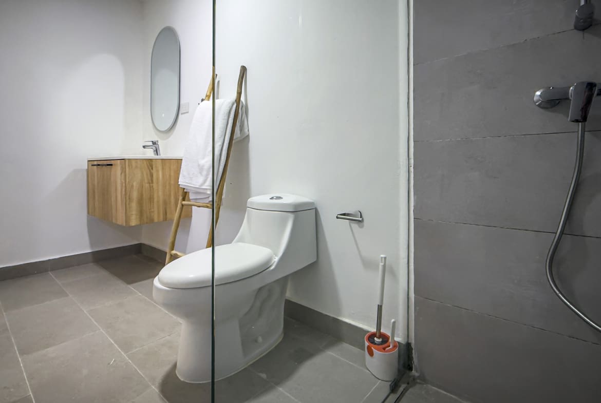 Modern bathroom with white toilet, wooden vanity, and grey tiled shower