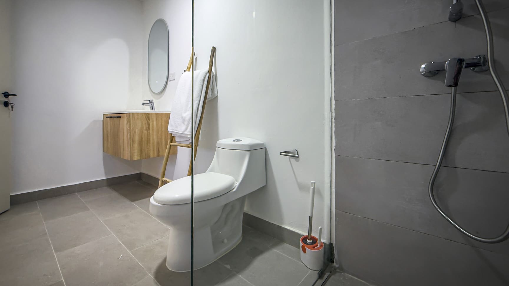 Modern bathroom with white toilet, wooden vanity, and grey tiled shower