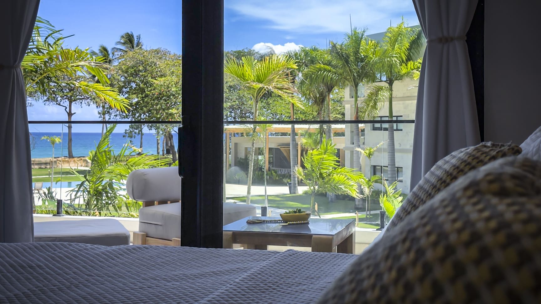 Luxury hotel room with ocean view, palm trees, and balcony.