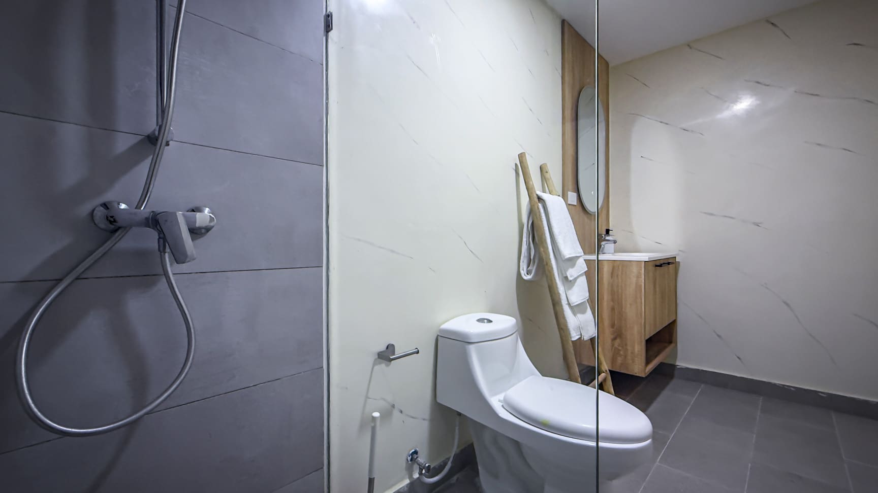 Modern bathroom with white toilet, wooden vanity, and grey shower