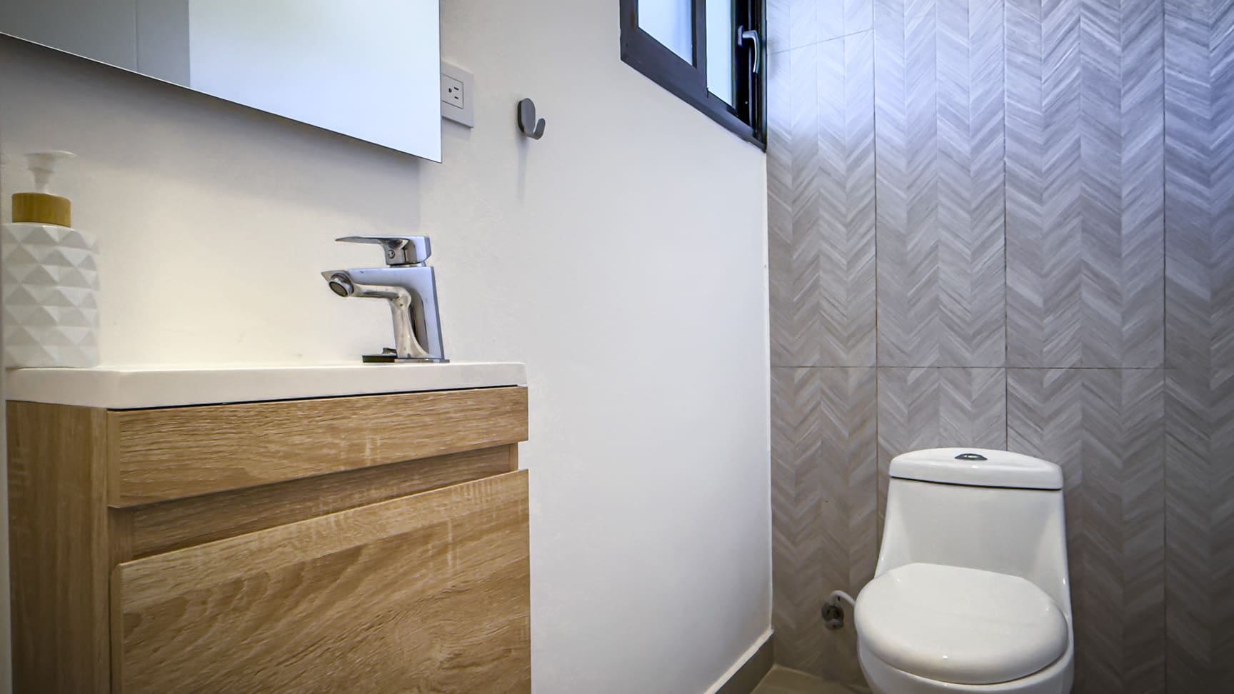Modern bathroom with wood vanity, chrome faucet, and patterned tile wall.