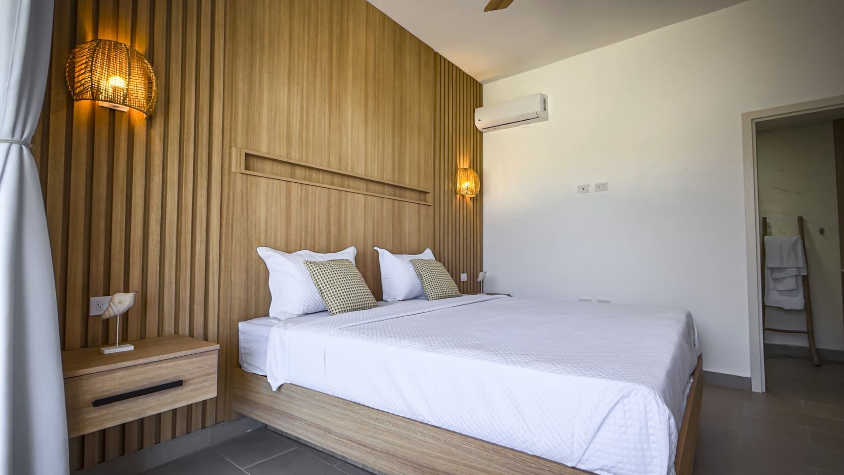 Modern bedroom with wooden accent wall, white bedding, and rattan lamps.